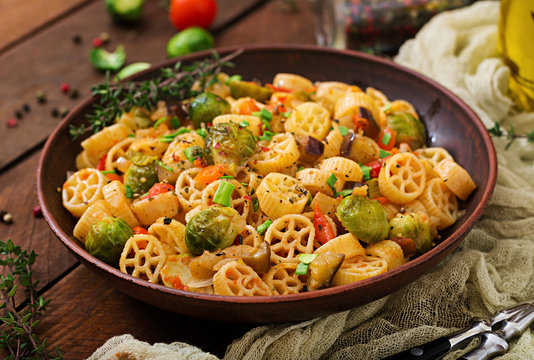 Vegetarian Vegetable pasta Rocchetti with brussels sprouts, tomato, eggplant and paprika in brown bowl on wooden table