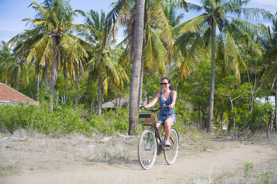 young happy and pretty Asian Chinese woman riding bike in Vietnam or Thailand tropical jungle forest with palm trees smiling relaxed