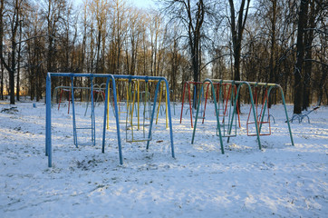 Swing at the deserted playground covered with snow in winter time and lit with the evening sun