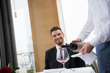 selective focus of waiter pouring red wine into wineglass in restaurant
