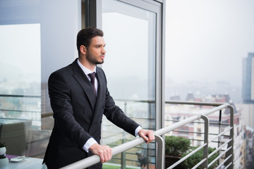 portrait of young pensive man in suit standing at balcony