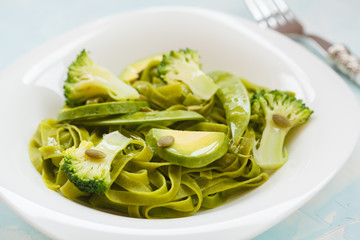 Healthy spinach pasta with broccoli, avocado, pumpkin seeds and green peas.