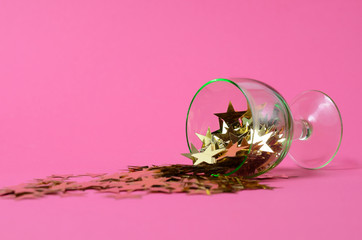 New Year party poster with still life of overturned wineglass with decorative stars on a pink background. Minimalistic concept