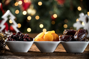 Dried apricots, pitted and dried berry in a bowl on the board with blurred christmas background