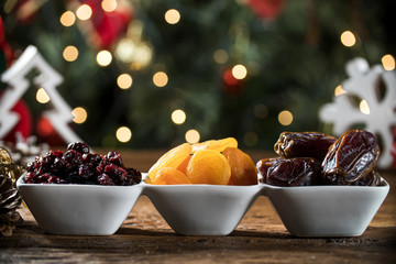 Dried apricots, pitted and dried berry in a bowl on the board with blurred christmas background