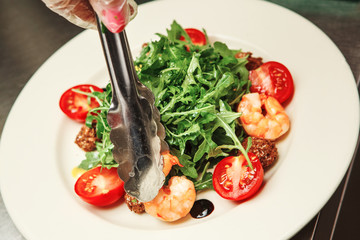Cook prepares salad with arugula, cherry tomatoes and sauce