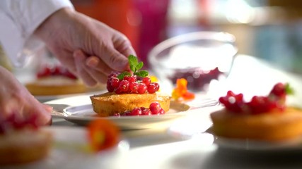 Close-up on the hands of the pastry chef decorating a cake with red currants and a mint leaf before serving.Video