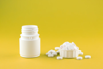 Close up white pill bottle with spilled out pills and capsules in cap on yellow lime background with copy space. Focus on foreground, soft bokeh. Pharmacy drugstore concept