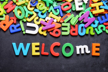 Welcome message written with colorful plastic letters on chalkboard or dark background