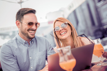 Happy couple using laptop in a coffee shop and having fun.