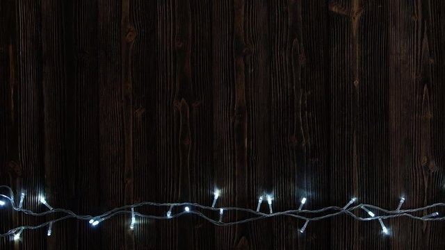 Fancy blinker light bulbs or garlands and wreath on wood table for Christmas or New years decoration background, Christmas colorful glowing lights border celebrate, add text or picture. 4K, UHD.