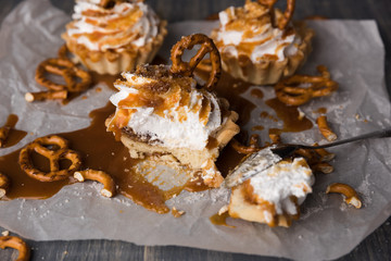 Homemade cupcakes with salted caramel and pretzels. Sweet cakes with syrup and cream cheese on baking paper and wooden table. Spoon