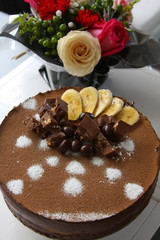 birthday bouquet of flowers chocolate and banana mousse cake decorated with cocoa powder, bananas, chocolate bars and candies on light background