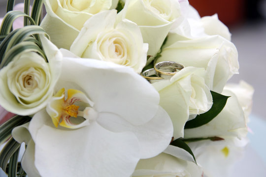 background of beautiful wedding bouquet of roses and orchids and two gold and platinum wedding rings