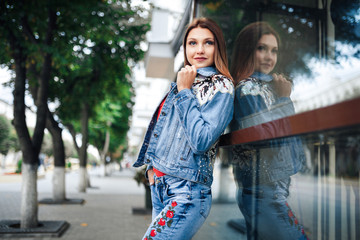 Young woman in blue jeans and red shirt standing in front of mirrored windows. Outdoor.