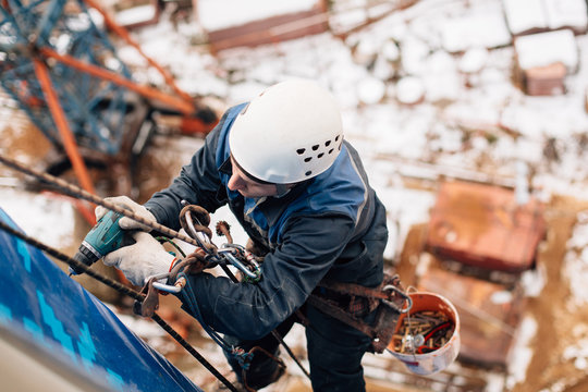 Professional industrial climber in helmet and uniform works at height. Risky extreme job. Industrial climbing at construction site