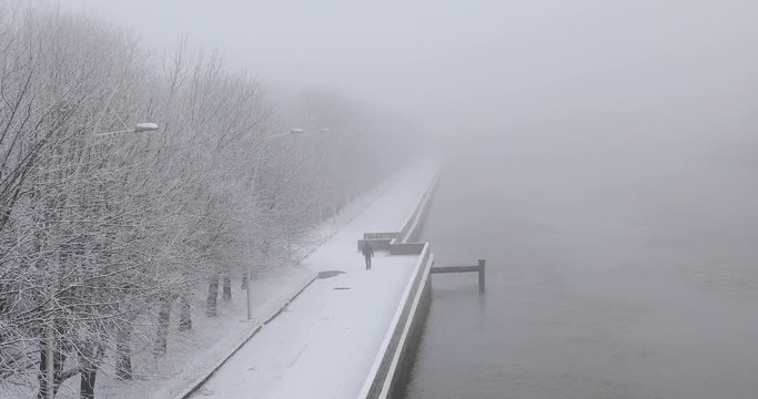 Man is walking along the riverbank in snowy winter