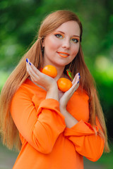 Portrait of pretty red hair woman with juicy delicious mandarins at summer green park.