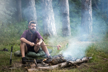 Man traveler roast sausages on stick on campfire in forest