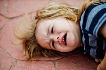 Kid boy with long blond hair cry on brown tile