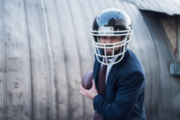 angry businessman in suit and rugby helmet with ball in hands on street