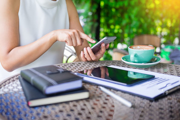 woman using smart phone and coffee beside on a wooden table in garden, warm sunlight.
