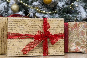 box with Christmas and new year gift in wrapping paper with a red ribbon under the Christmas tree