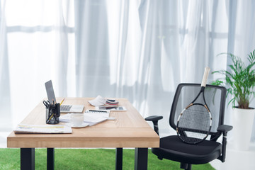 close up view of workplace with laptop and tennis racket in office