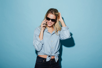 Happy blonde woman in shirt and sunglasses talking by smartphone