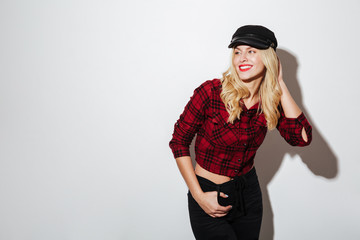 Happy blonde woman in checkered shirt and cap posing