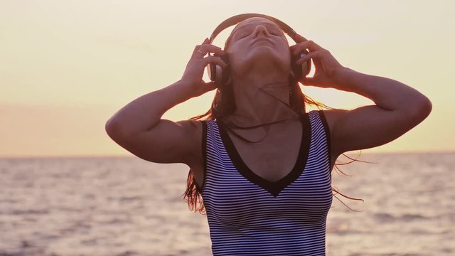 Young pretty woman have fun listening music in headphone on the beach at amazing sunset in slow motion 180fps. 1920x1080