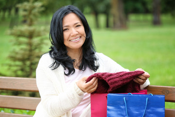 Beautiful mature woman taking clothes out of shopping bag outdoors