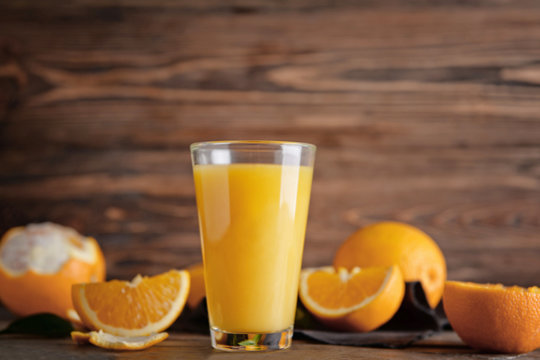 Glass of fresh juice and oranges on wooden background