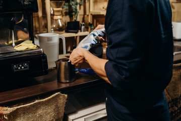 Handsome barista preparing cup of coffee for customer in coffee shop. Retro picture with little noise.