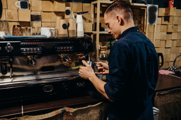 Handsome barista preparing cup of coffee for customer in coffee shop. Retro picture with little noise.