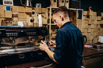 Handsome barista preparing cup of coffee for customer in coffee shop. Retro picture with little noise.