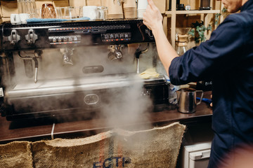 Handsome barista preparing cup of coffee for customer in coffee shop. Retro picture with little noise.
