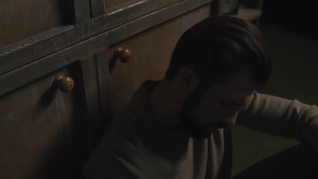 Loneliness. Close up of bearded man feeling lonely while sitting on the floor and drinking alcohol