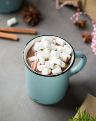 Mug of hot chocolate with marshmallow and cinnamon on a gray concrete background with a Christmas tree, gifts. and red-white string (twine). Winter xmas holidays concept. Festive mood.