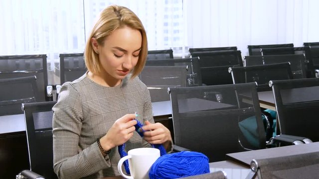Young woman knitting at working place wearing headphones and smile. Leisure time at office concept. Businesswoman procrastinate