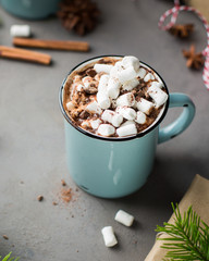 Great things will be served!) Mug of hot chocolate with marshmallow, cinnamon and milk on a gray concrete background with a Christmas tree and gifts. Winter xmas holidays concept