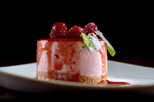 Close-uf a delicious souffle dessert decorated with raspberies and fresh mint leaves, served on white square plate. Photo was taken on black background. Tasty for sweet buffet or catering.