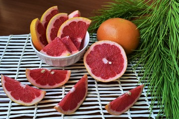 Red grapefruit slices i a bowl and on a wicker mat, Christmas tree branch.