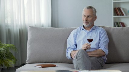 Happy adult person sitting on sofa, drinking red wine and thinking about life