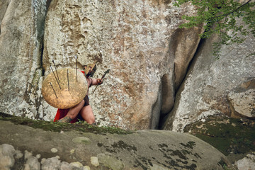 Low angle full length shot of an armored Spartan soldier covering himself with a shield from enemies archers copyspace war fight conflict protection defensive safety bravery masculinity weapon.
