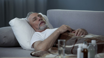 Obraz premium Male in his 60s sleeping in bed at home, pills and fluids standing on the table