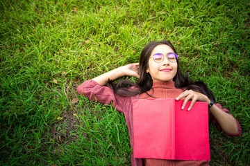 Portrait of high school girl lay down and read a book in park, education concept