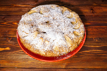 Apple pie sprinkled with powdered sugar on the background of a dark board.
