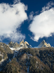 Clouds swirling around steep, rocky mountain peaks in the Alps with snow on the trees below the mountains