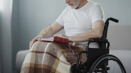 Sad adult man with disabilities reviewing album with photos, missing relatives